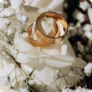 Złote obrączki ślubne ułożone na białych różach z delikatnymi kwiatami gipsówki, nadające elegancji i romantyzmu.